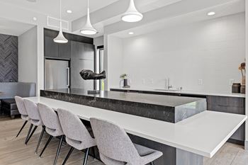 A modern kitchen with a marble countertop and grey chairs.